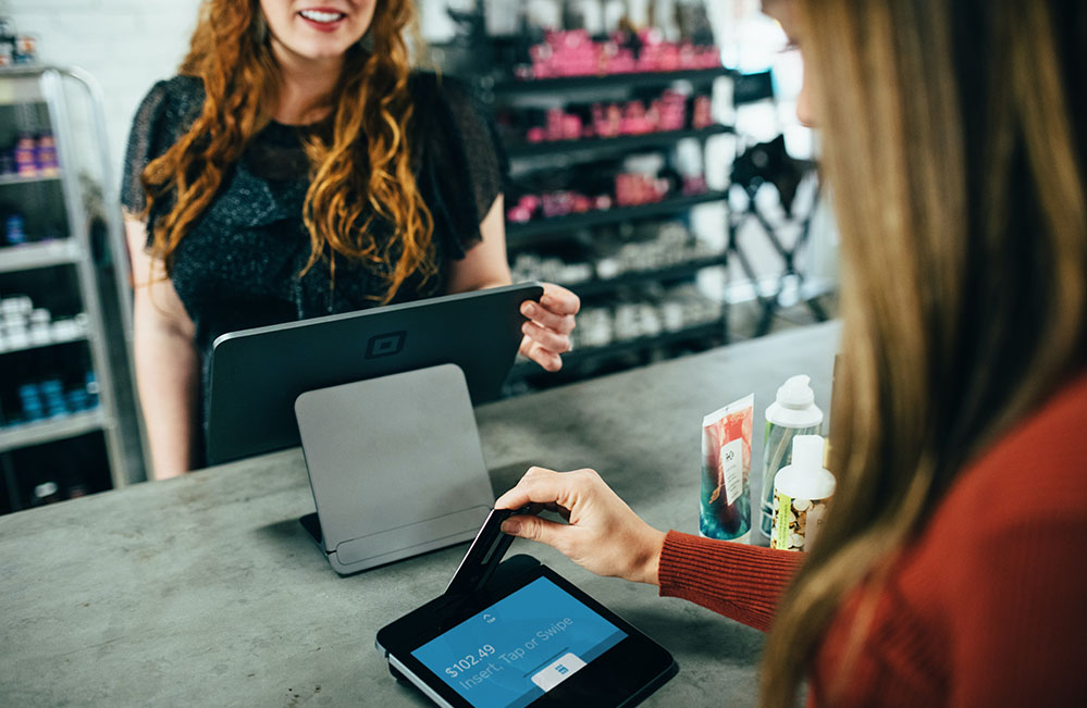 Female customer swiping credit card, while female cashier smiles.